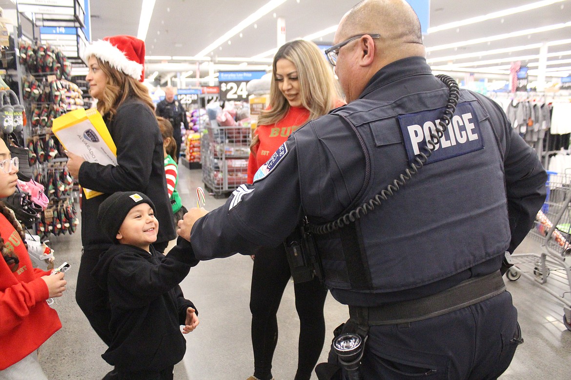 A Moses Lake Police Department officer hands out a candy cane to a passing child during Shop With a Cop Tuesday.