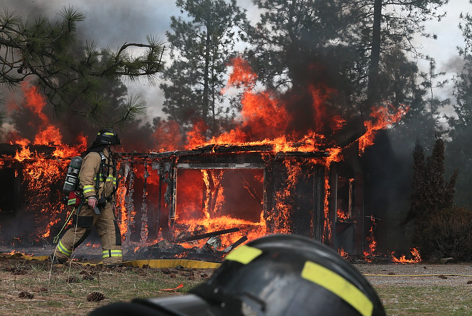 Hauser Lake Fire Protection District firefighter Kyle Andrews walks by a burning house April 22 at a training site at Highway 53 and Pleasant View Road.