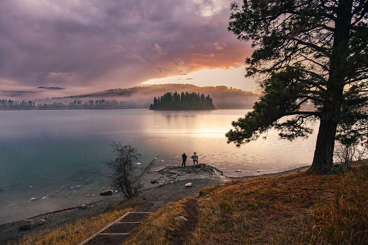 Kristina Ramirez and Jesse Good watch as the sun peeks out from a layer of clouds before dipping below the horizon at Foys Lake on Friday, Dec. 22. (Casey Kreider/Daily Inter Lake)