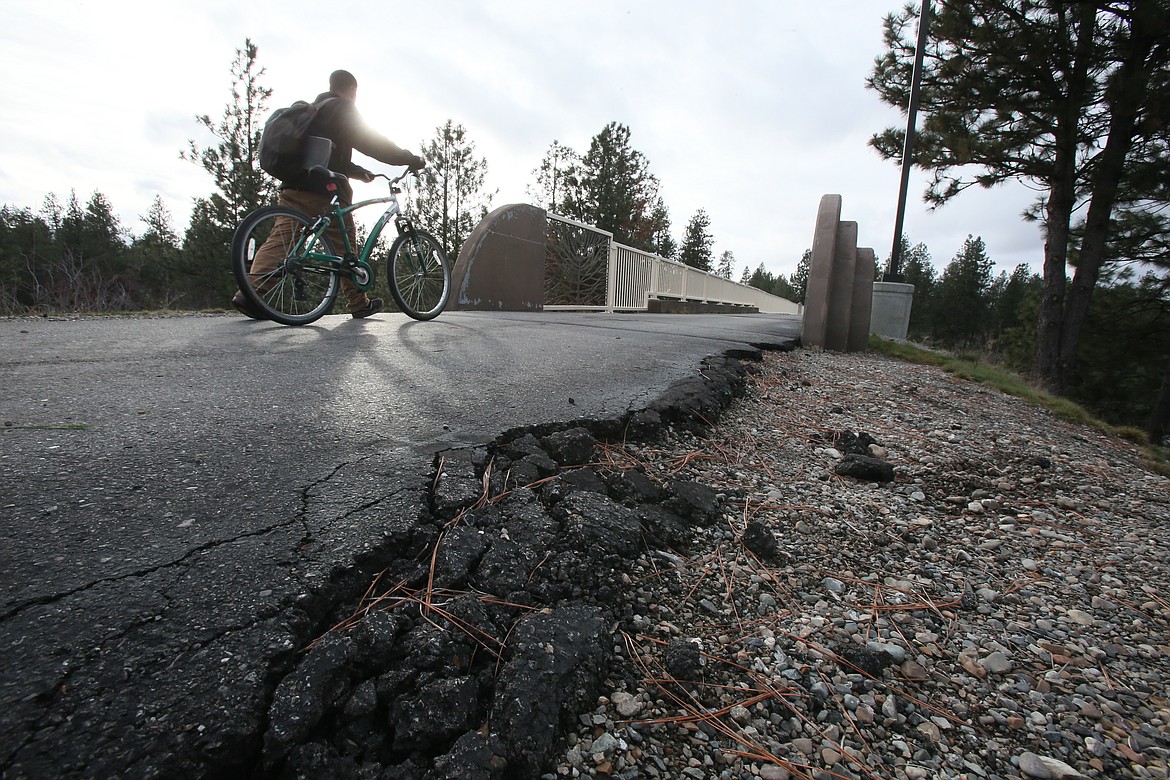 A trail user rides near a crumbling asphalt edge Friday on the North Idaho Centennial Trail.