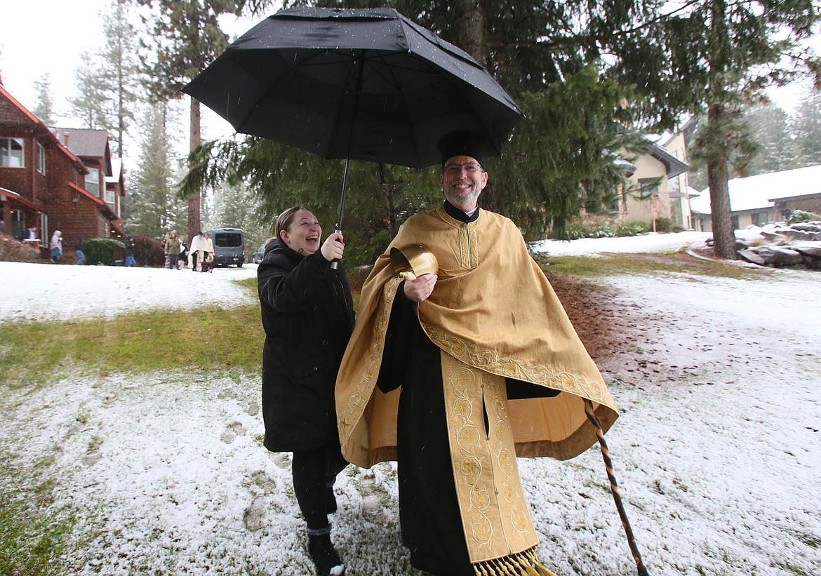 Tabitha Townsend holds an umbrella for her dad, the Rev. Mark Townsend, as the two share a laugh Saturday on their way to the Spokane River for a Theophany water blessing ceremony.