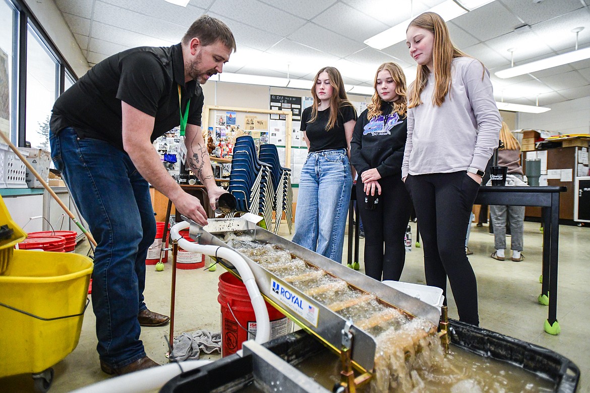 Kalispell Middle School teacher Kris Schreiner demonstrates how to use a sluice to eighth-graders, from left, Shyann Richsel, Kaylee Whitten and Hallie Granley during a lesson on panning for gold, garnets and other minerals in his history class on Tuesday, Jan. 16. (Casey Kreider/Daily Inter Lake)