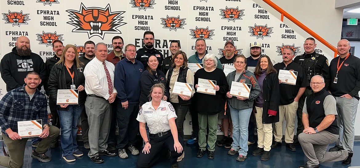 Eleven Ephrata High staff, holding certificates, pause for a photo with Ephrata School District board members and administrators as well as first responders. They were recognized with Excellence Awards from the district for their actions that saved the life of an unidentified staff member.