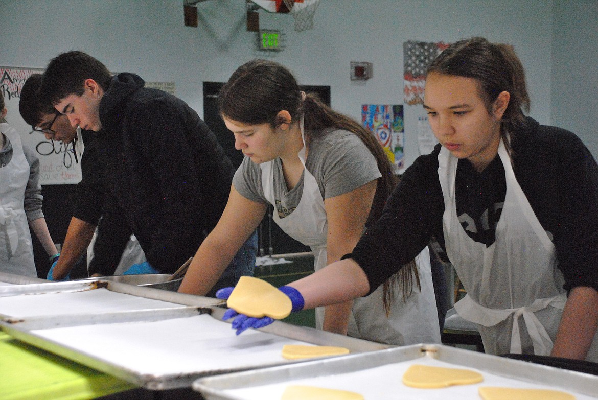 Zaylee Simkins, right, places a heart-shaped cookie onto a baking sheet Saturday at the St. Regis Cafeteria. Fellow BPA members, Mae Grosenbaugh, and Jack Connolly roll out and cut dough. (Mineral Independent/Amy Quinlivan)