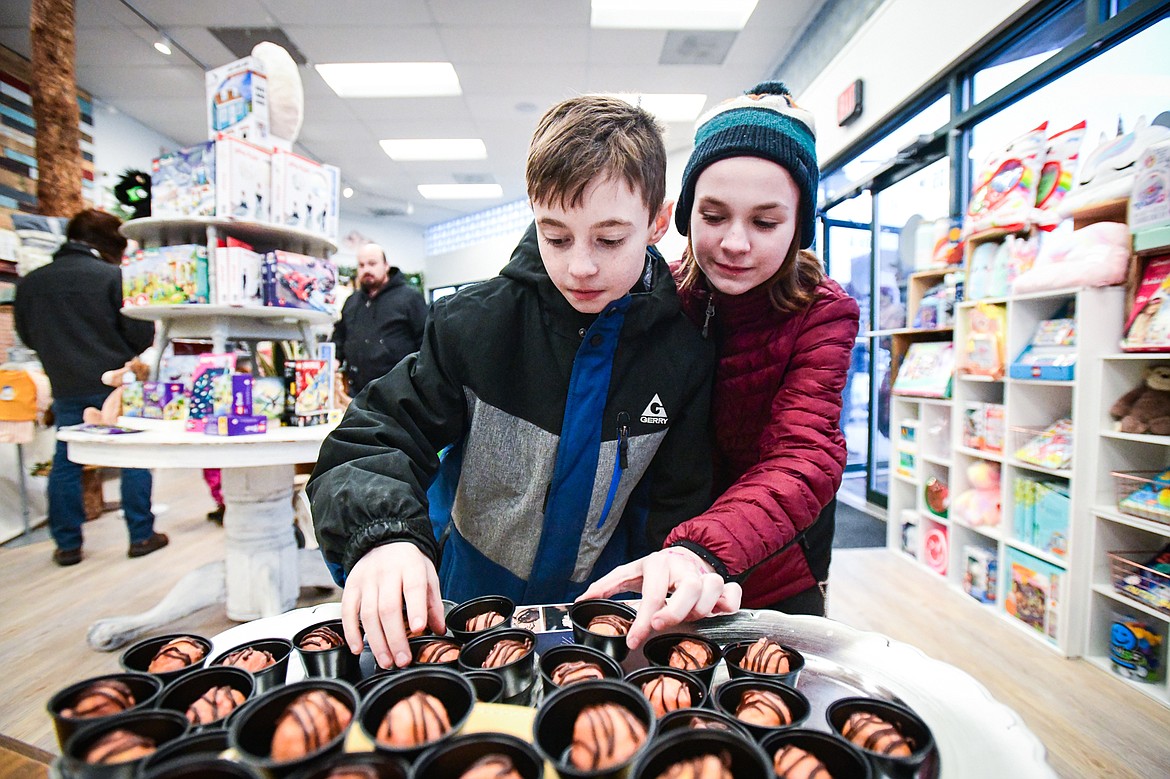 Diezel Campbell and Eloise Brown grab a  strawberry and chocolate donut hole made by The Spot at Nature Baby Outfitter during the 2024 Chocolate Affair in downtown Kalispell on Friday, Feb. 9. (Casey Kreider/Daily Inter Lake)