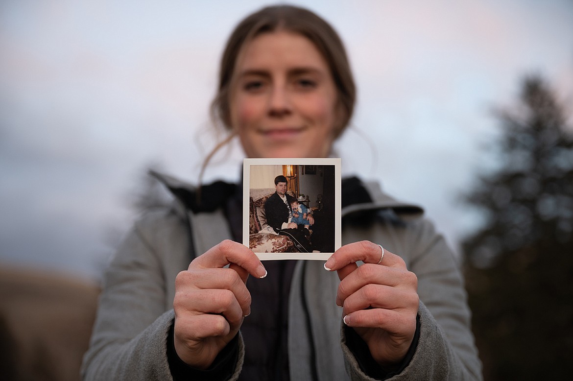 Teigan Avery poses for a portrait at the University of Montana, where she completed her undergraduate degree and graduated with a master’s in economics. She holds a photograph of herself and her father, Jerad Avery, from her childhood. (Ava Rosvold/UM Byline Magazine)