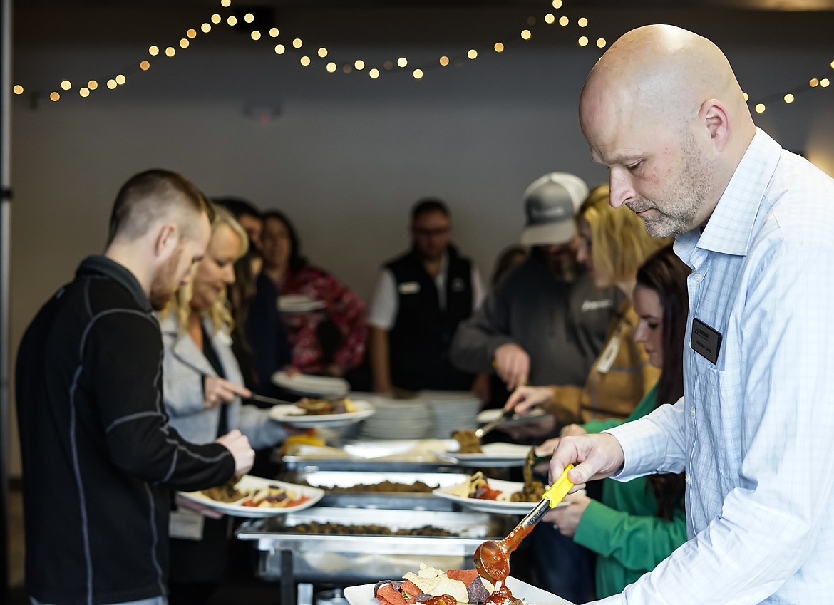 Matthew Davis with the Fairway Independent Mortgage Corporation and other guests grab a plate of food during the Tuesday Post Falls Chamber of Commerce luncheon at The Club in Post Falls.