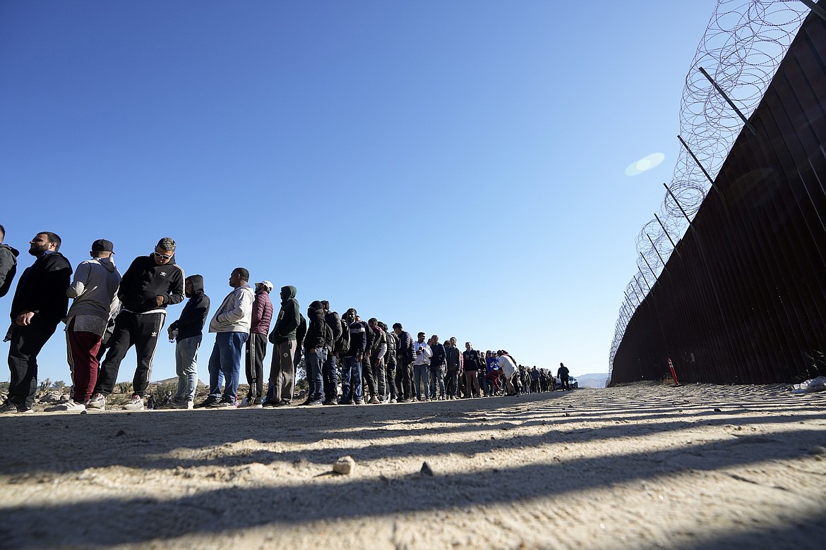 Men line up to receive food from volunteers with Border Kindness after crossing the border with Mexico Tuesday, Oct. 24, 2023, near Jacumba, Calif. President Joe Biden is trying to sweeten his pitch for more money for Ukraine by mixing in billions of dollars for securing the U.S.-Mexico border in the hope that it will bring more Republicans on board. (AP Photo/Gregory Bull)