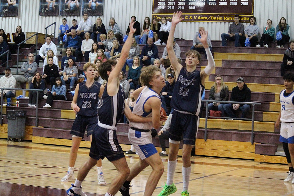 Soap Lake junior Ruvim Goloborodko, in white, keeps his eyes on the rim while being defended by Summit Classical Christian players.