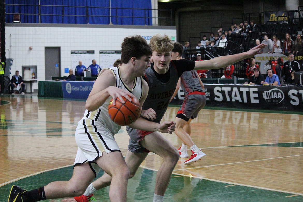 Royal senior Bennett Brown, in white, dribbles the ball toward the rim against Riverside at the 1A Boys State Basketball Tournament.