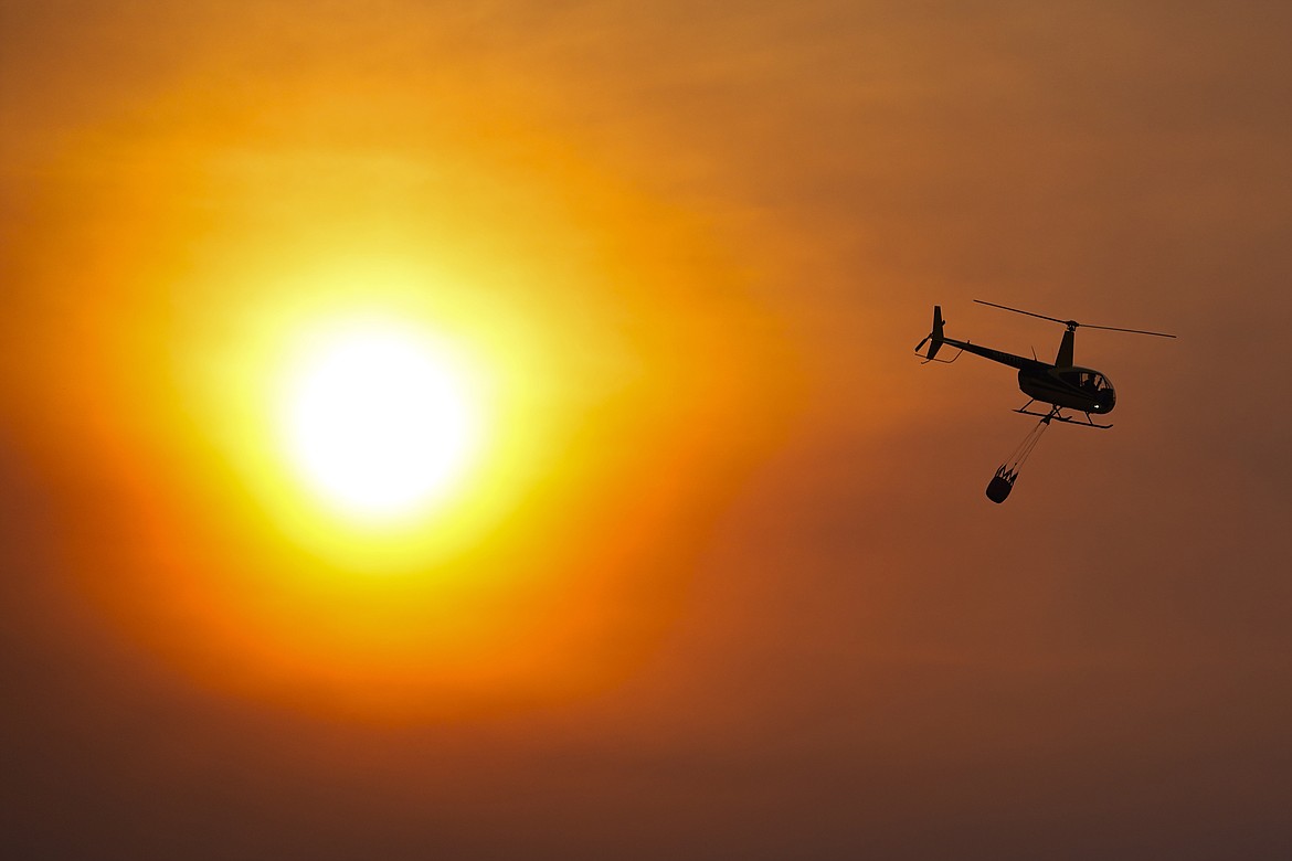 A helicopter carries a bucket as it flies over homes burned by the Smokehouse Creek Fire, Wednesday, Feb. 28, 2024, in Canadian, Texas. (AP Photo/Julio Cortez)