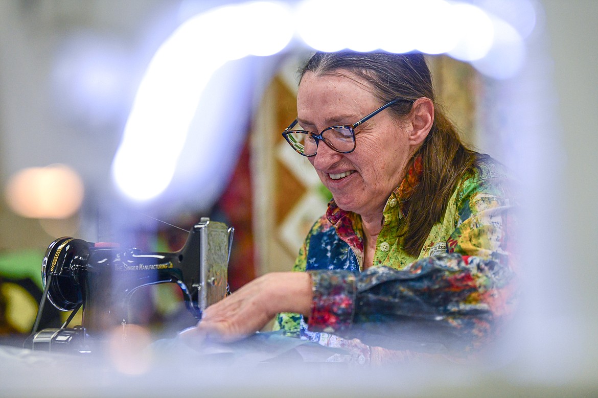 Flathead Quilters' Guild member Cathy Calloway stitches together individual quilt blocks on her Singer Featherweight sewing machine from the 1930s, viewed through the lighted arm of a Husqvarna Viking Mega Quilter sewing machine, during one of the Guild's sewing days at the Quilt Gallery in Kalispell on Wednesday, March 13. (Casey Kreider/Daily Inter Lake)