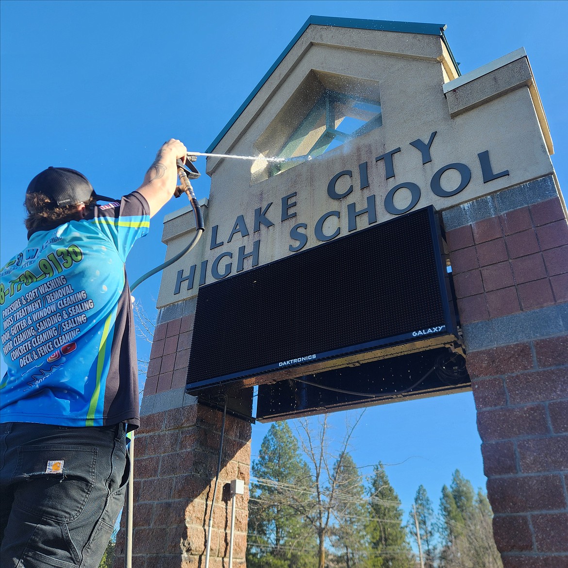 Dylan Cederburg, co-owner of Eco-Wash LLC, uses a soft wash March 18 to clear organic material from Lake City High School's exterior sign. Cederburg and business partner Josh Ribble donated their services as a way to give back to the school they once attended.