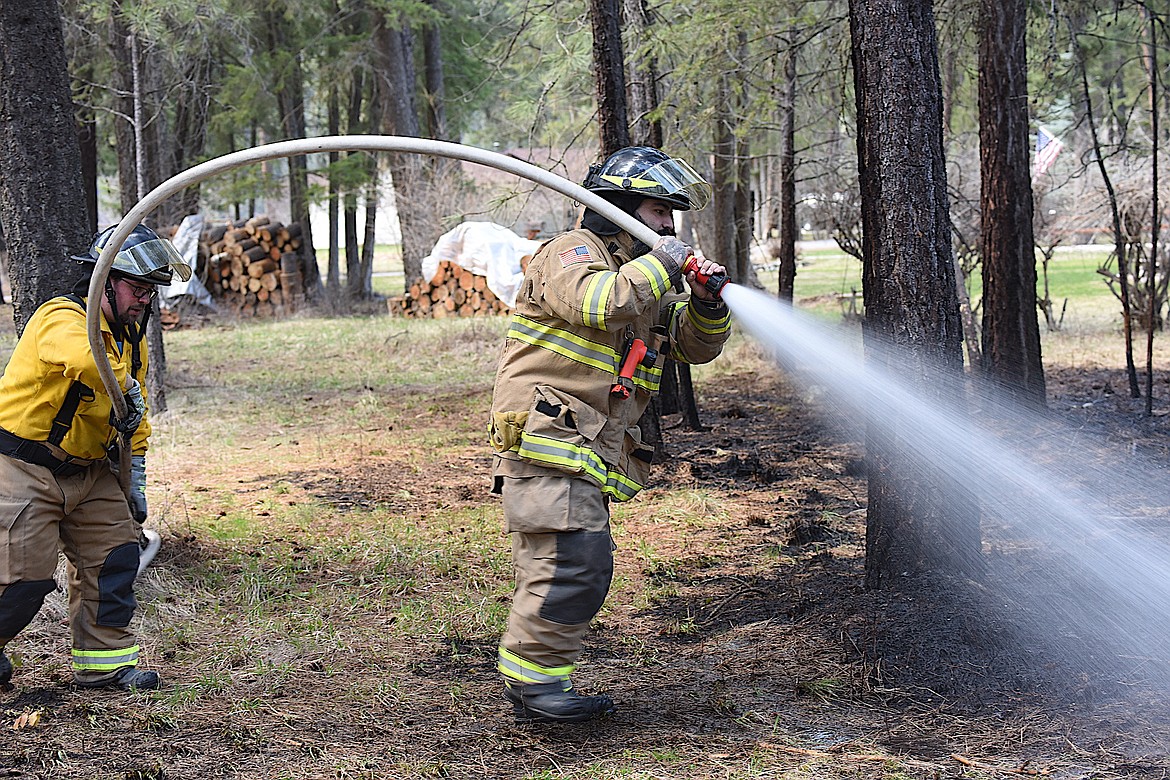 Two firefighters from Lincoln County Rural Fire District 1 spray water on a hot spot from a small brush pile fire Tuesday afternoon in Em Kayan Village. (Scott Shindledecker/The Western News)