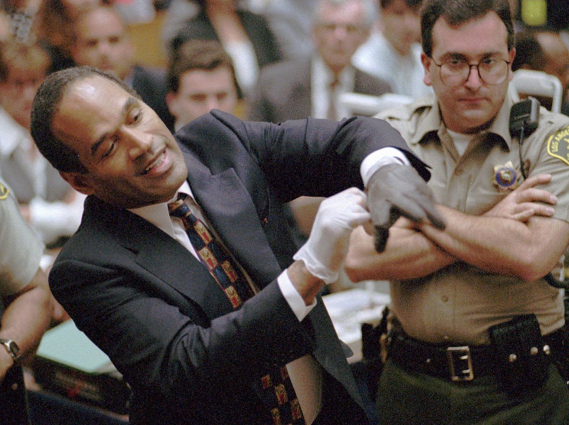 In this June 15, 1995 file photo, O.J. Simpson, left, grimaces as he tries on one of the leather gloves prosecutors say he wore the night his ex-wife Nicole Brown Simpson and Ron Goldman were murdered in a Los Angeles courtroom. Simpson, the decorated football superstar and Hollywood actor who was acquitted of charges he killed his former wife and her friend but later found liable in a separate civil trial, has died. He was 76. (Sam Mircovich/Pool Photo via AP, File)