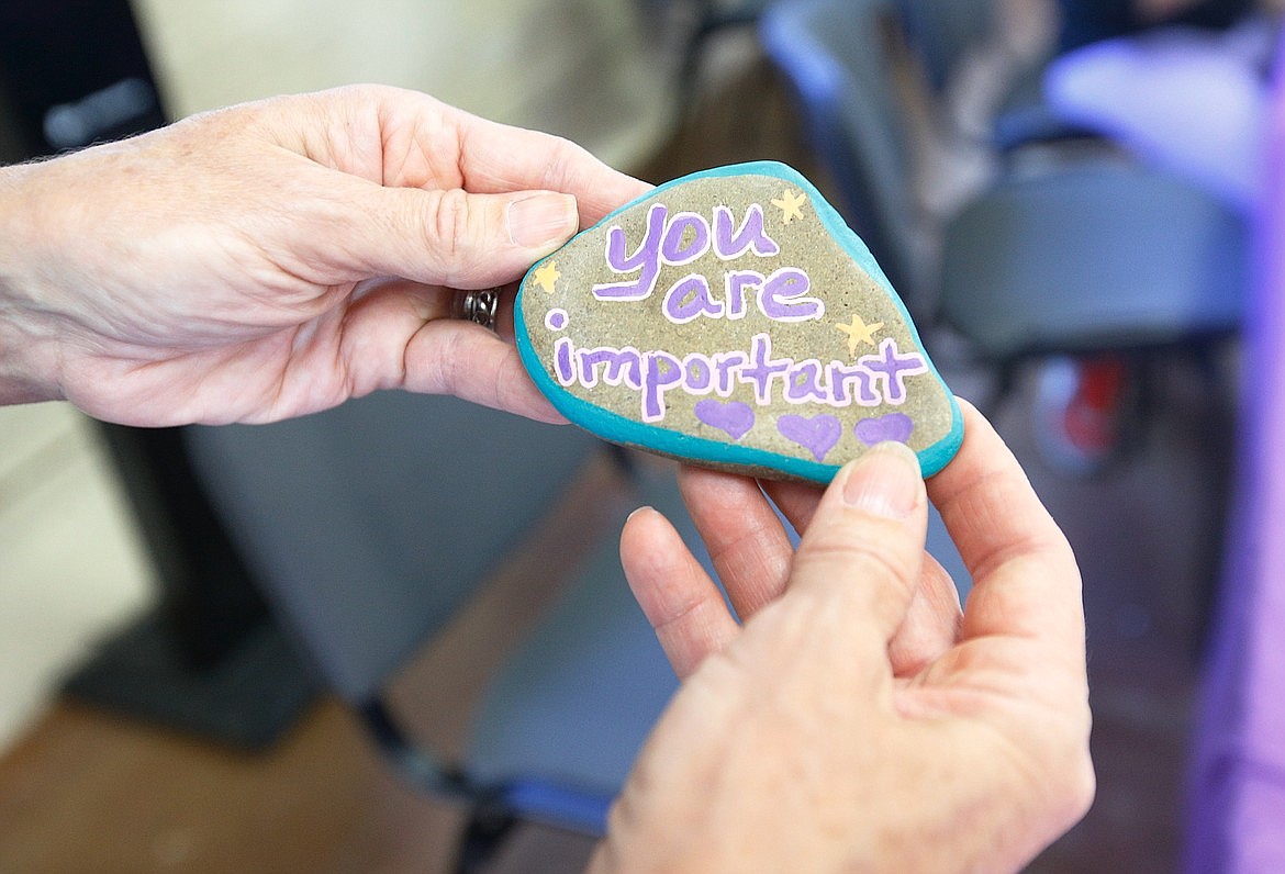 Leslie Johnson holds a rock painted with a positive message on one side and information for Safe Passage Violence Prevention Center on the back.