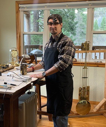 Surrounded by clocks, gears, and movements, Christopher Anderson is happily at work as a Horologist in his home in St. Regis. He wears magnifying loupes over his glasses to do very small detailed work on timepieces he repairs and maintains. (Photo courtesy/Christopher Anderson)