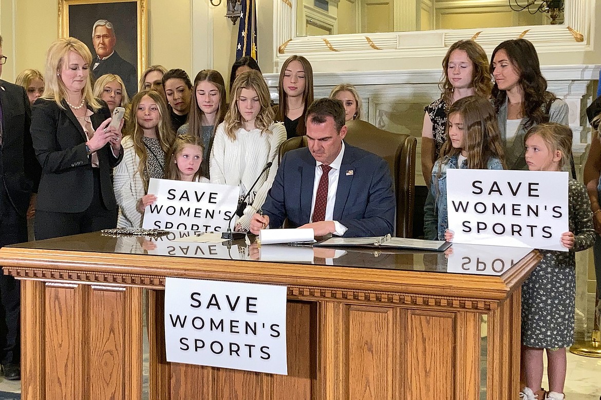 Oklahoma Gov. Kevin Stitt, center, signs a bill that prevents transgender girls and women from competing on female sports teams, March 30, 2022, in Oklahoma City. A new rule from President Joe Biden's administration assuring transgender students be allowed to use the school bathrooms that align with their gender identity could conflict with laws in Republican-controlled states that seek to make sure they can't. (AP Photo/Sean Murphy, File)