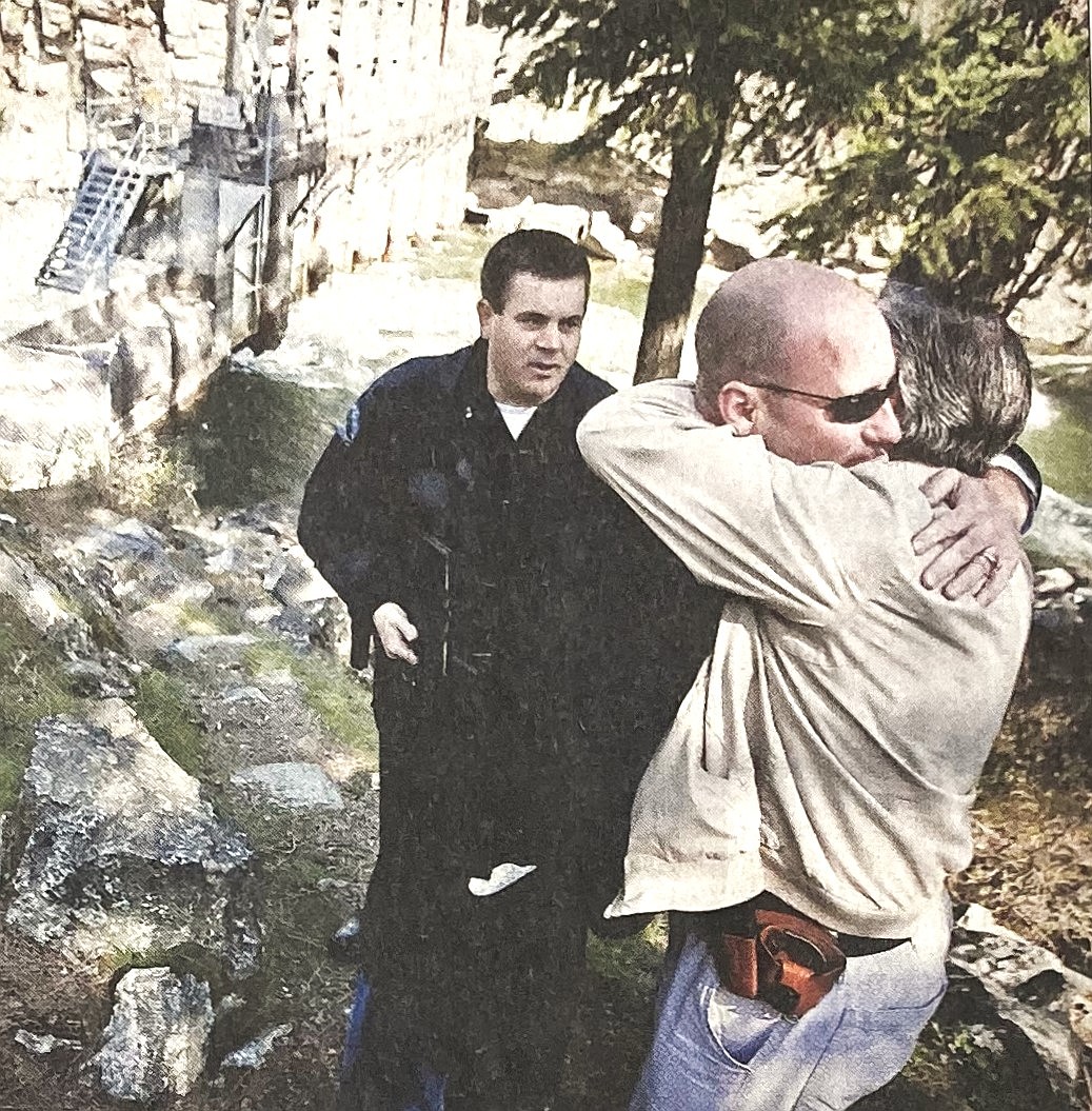 Survivor Bob Pearl (sunglasses) hugs Deputy Gary Dagastine, while Scot Haug of the Post Falls Police Department watches near the Post Falls Dam.