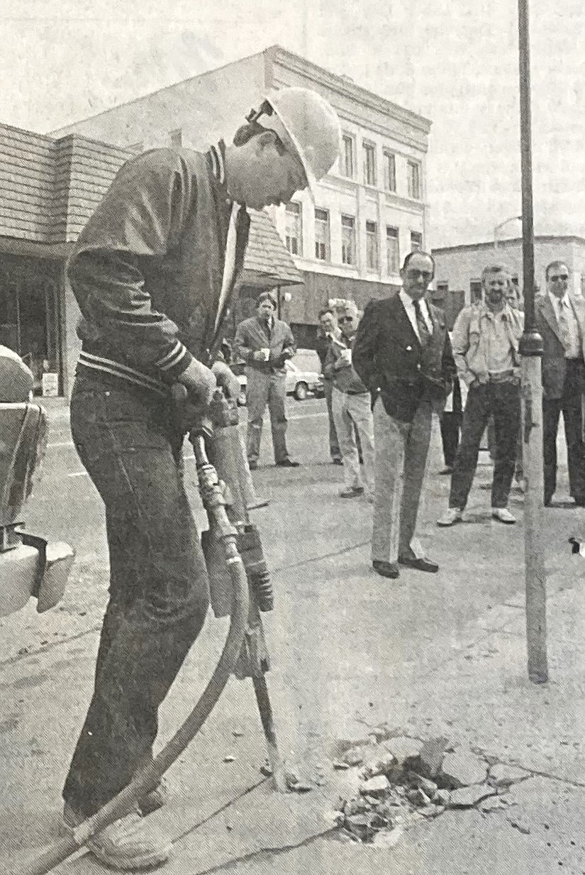 Frank Gabriel of Norm’s Electric jackhammers concrete to launch 1989 downtown revitalization project, while Mayor Ray Stone and others watch.