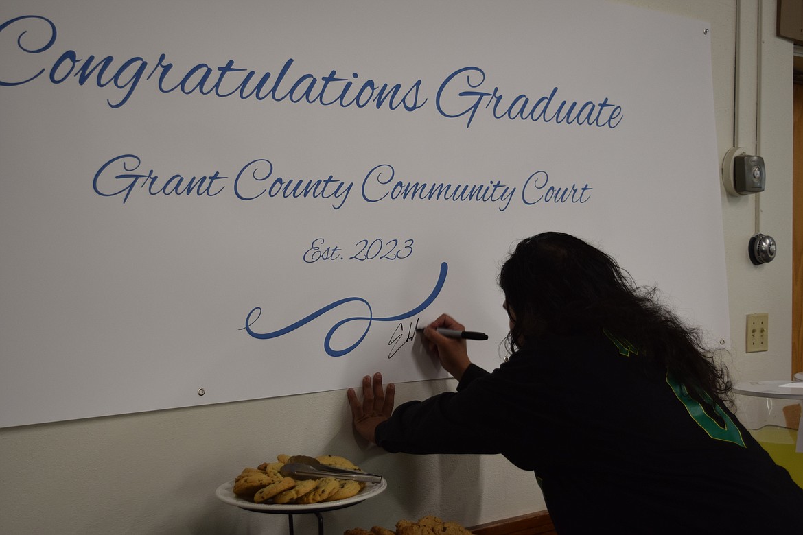 Eddie Navarro signs a graduation banner after completing his requirements to graduate. District Court Judge Brian Gwinn, who presides over Community Court, said he hopes Navarro's leadership and example will help to turn the banner black with sharpied signatures in the years to come.