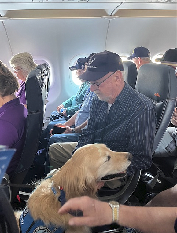 Joe Deacon reads during his Honor Flight while Isaac the comfort dog stands guard.