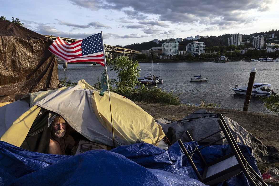 Frank, a homeless man sits in his tent with a river view in Portland, Ore., Saturday, June 5, 2021. The city council in Portland, Oregon, has approved new homeless camping rules. Under the rules, people who reject offers of shelter can face penalties, including fines of up to $100 or up to seven days in jail. (AP Photo/Paula Bronstein, File)