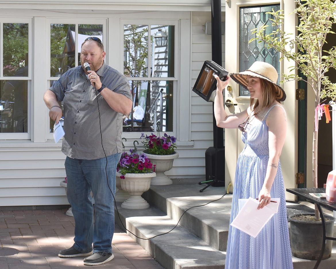 Columbia Basin Allied Arts Director Shawn Cardwell, right, holds up part of a Seahawks game package as auctioneer Chuck Yarbro Jr. takes bids at the CBAA Garden Party auction Saturday. The package, which included game tickets, parking and collectibles, sold for $2,200.