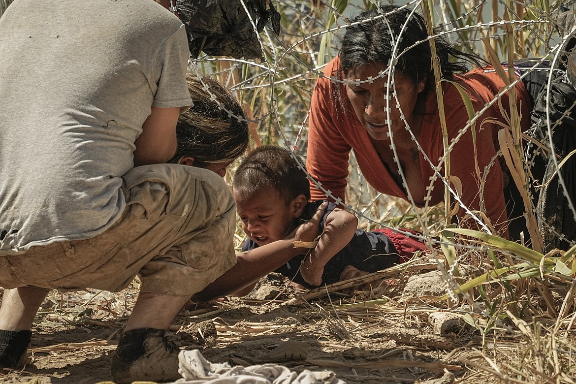 Migrants who crossed into the U.S. from Mexico pass under concertina wire along the Rio Grande river, Thursday, Sept. 21, 2023, in Eagle Pass, Texas. (AP Photo/Eric Gay)