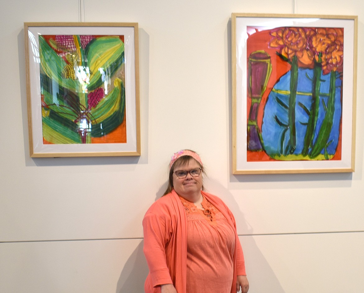 Artist Beth Anna Margolis stands between two of her paintings: “Flower Bud,” left, and “Blue Light.” “Blue Light” was inspired by a friend who had a collection of blue glass vases. “She’d set them in the window and the light would come through,” Margolis said.