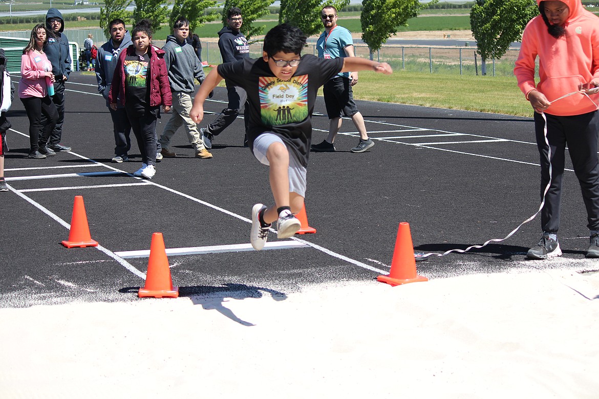 A participant flies in the air at the long jump pit at Field Day.