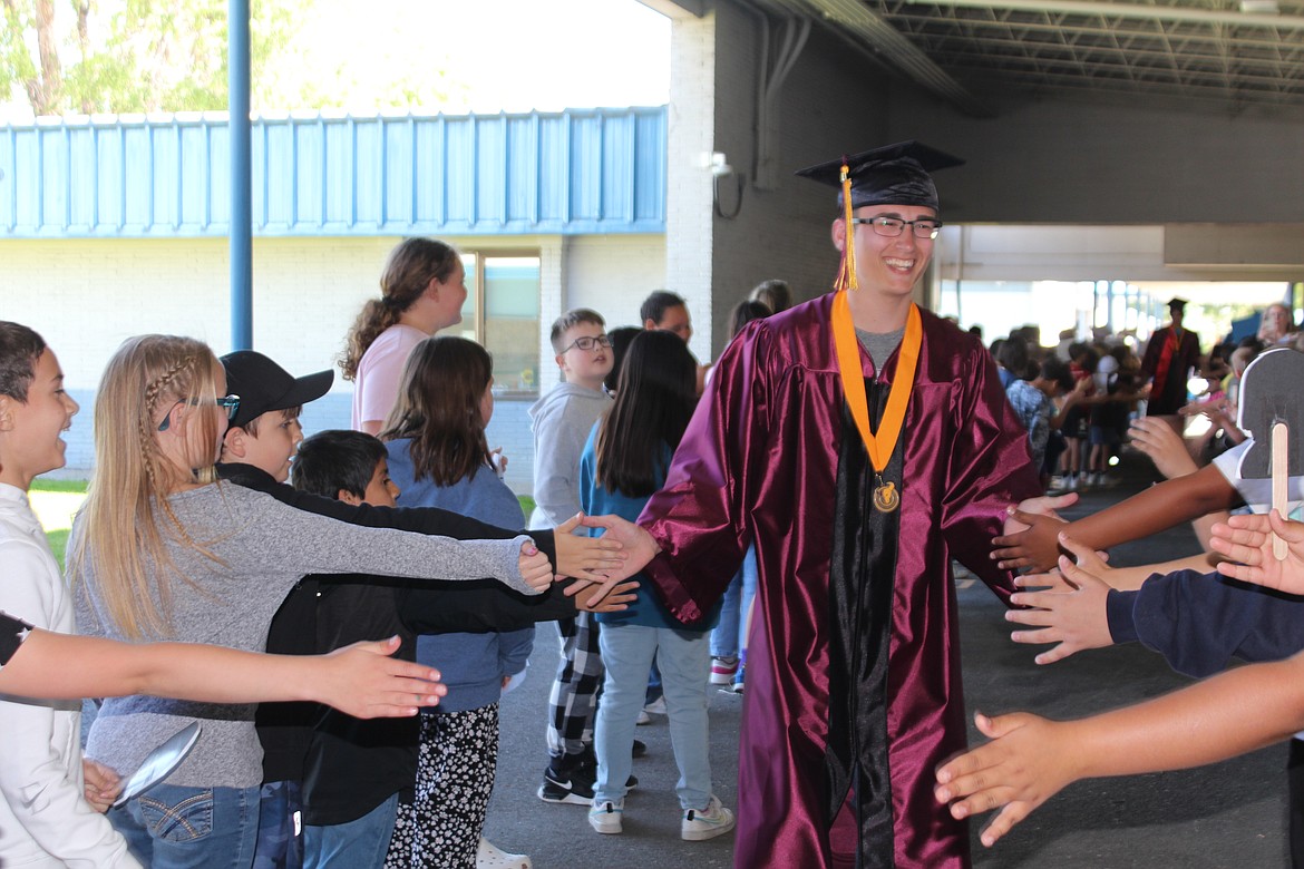 A Moses Lake High School graduate walks through a forest of outstretched hands at Peninsula Elementary.