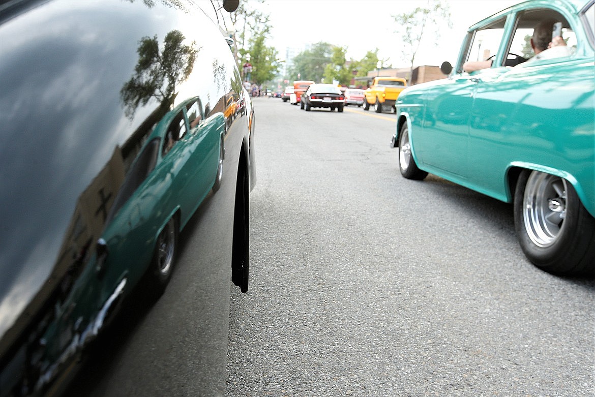 A classic car is reflected in the polished fender of another beauty as it cruises during Car d'Lane 2023.