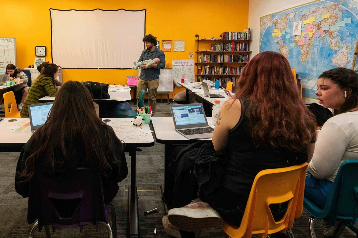 History teacher Trevor Bradley holds a student’s baby while his class completes coursework at Lumen High School.