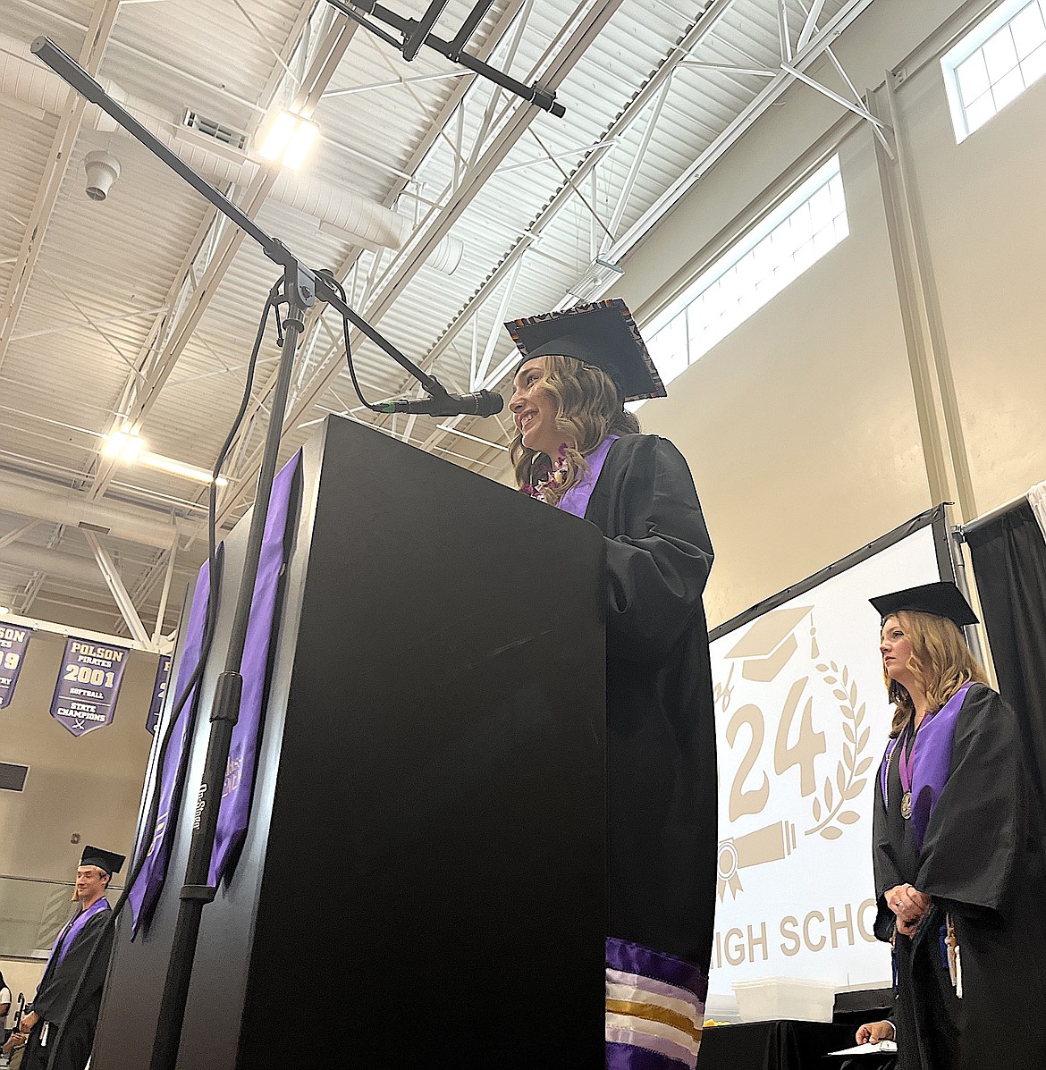 THE TURNING OF THE TASSELS: Valedictorian Julia Barnard (at the podium), flanked by Kai McDonald (left) Ashley Maki (right) prepares Polson graduates to flip their tassels from right to left – signifying their final step between high school and whatever comes next. (Kristi Niemeyer/Leader)