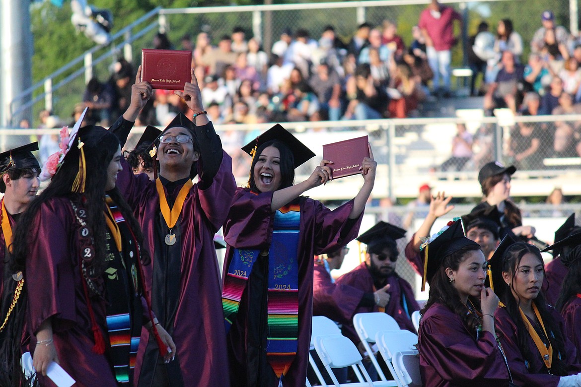 Two graduates in the Moses Lake High School class of 2024 show their brand-new diplomas to family and friends in the stands.