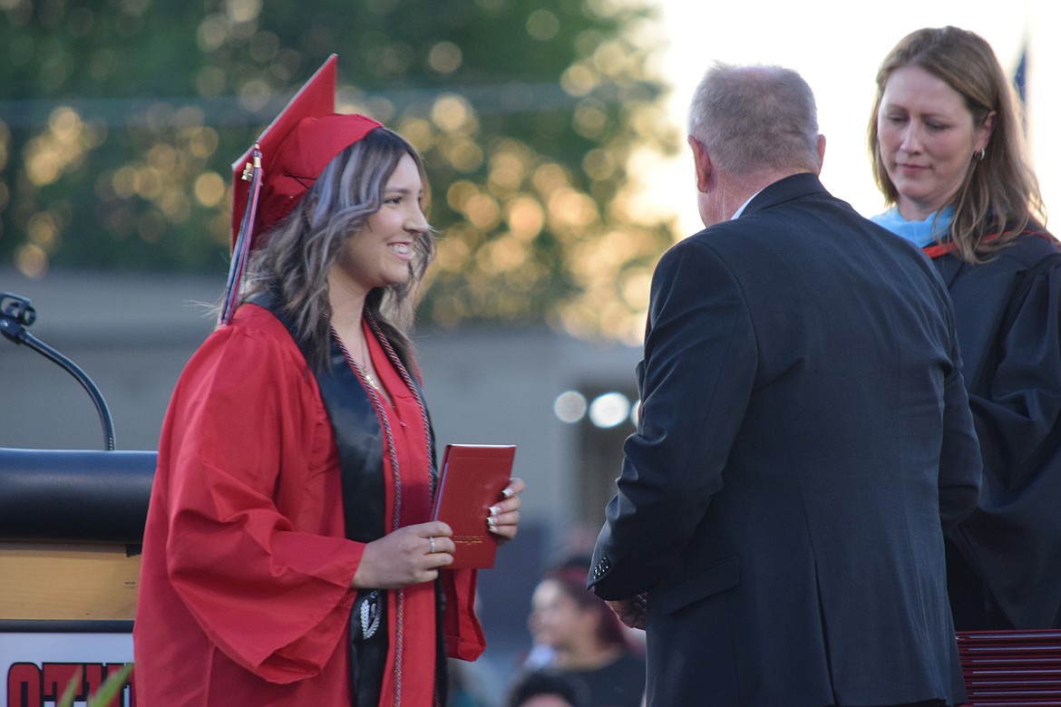 A member of Othello’s Class of 2024 accepts her diploma during the graduation ceremony outside Othello High School.