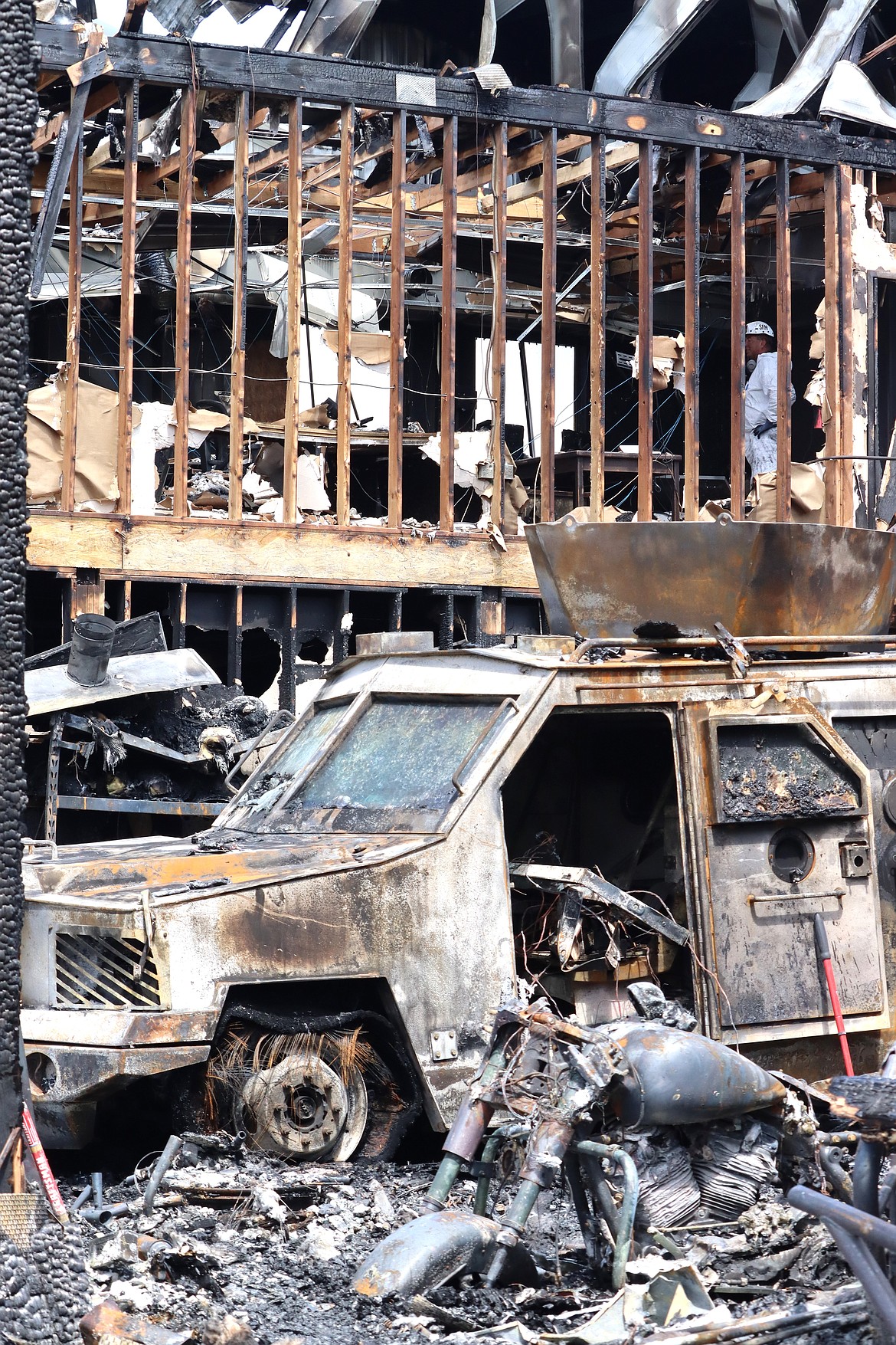 An investigator in a white suit stands on a second floor of the city building destroyed in a fire on Sunday, while the remains of a SWAT Bearcat vehicle sit on the ground level on Monday.