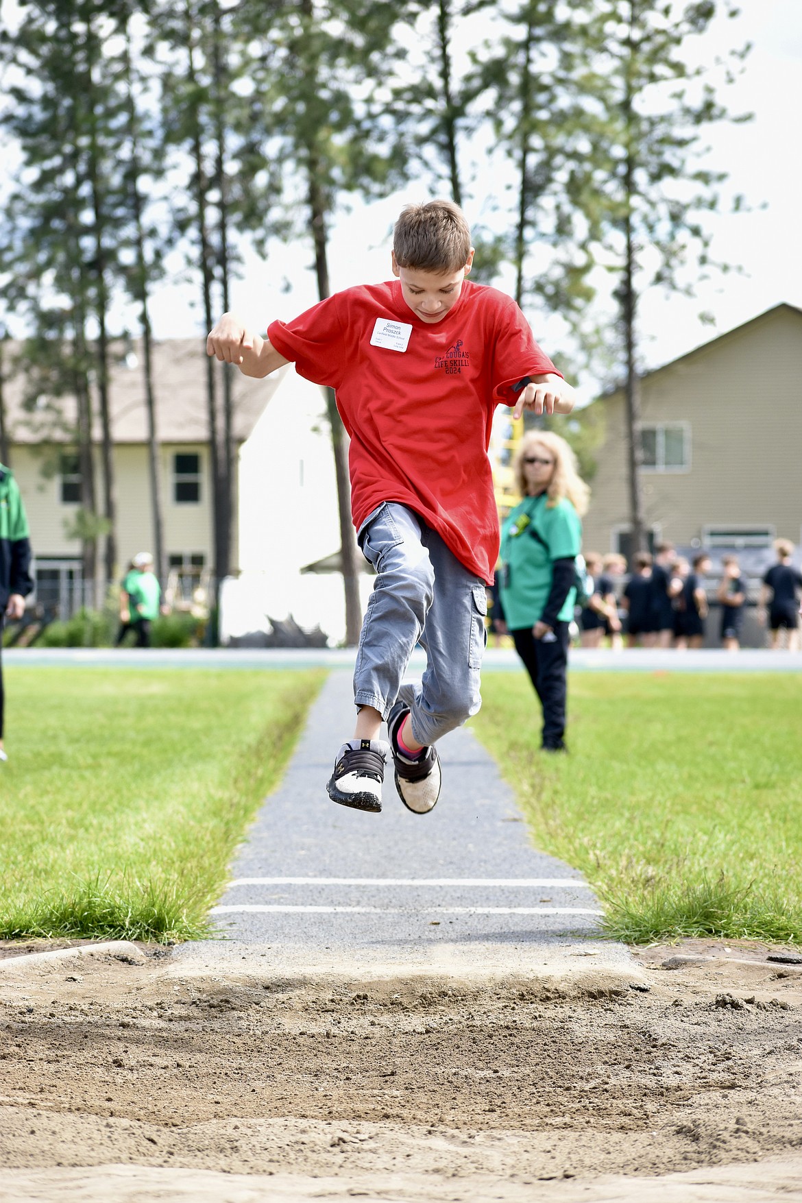 Simon Proszek of Canfield Middle School takes a leap as part of the long jump. Behind him, paraprofessional Wanda Hendrickson watches his jump as she oversees the long jump event at the life skills track event.