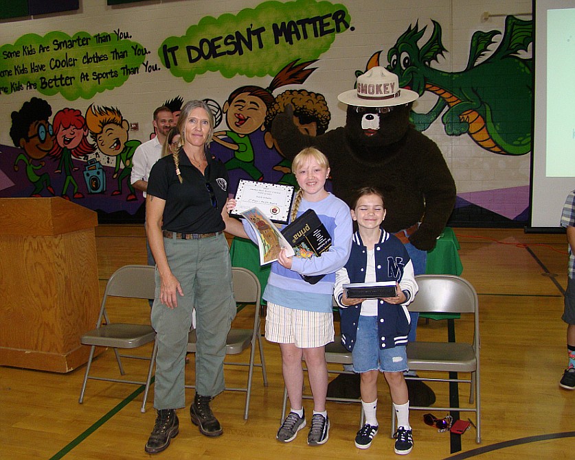 Jenna Nipp from the Forest Service and Smokey Bear presented certificates and drawing kits to Dalton Elementary fifth grader Faith Schultz, center, and fourth grader Claire Facciano during a presentation Friday morning. The students were first-place winners in Idaho and second-place winners in the Pacific Region for the National Garden Clubs, Inc. Smokey Bear and Woodsy Owl Poster Contest.