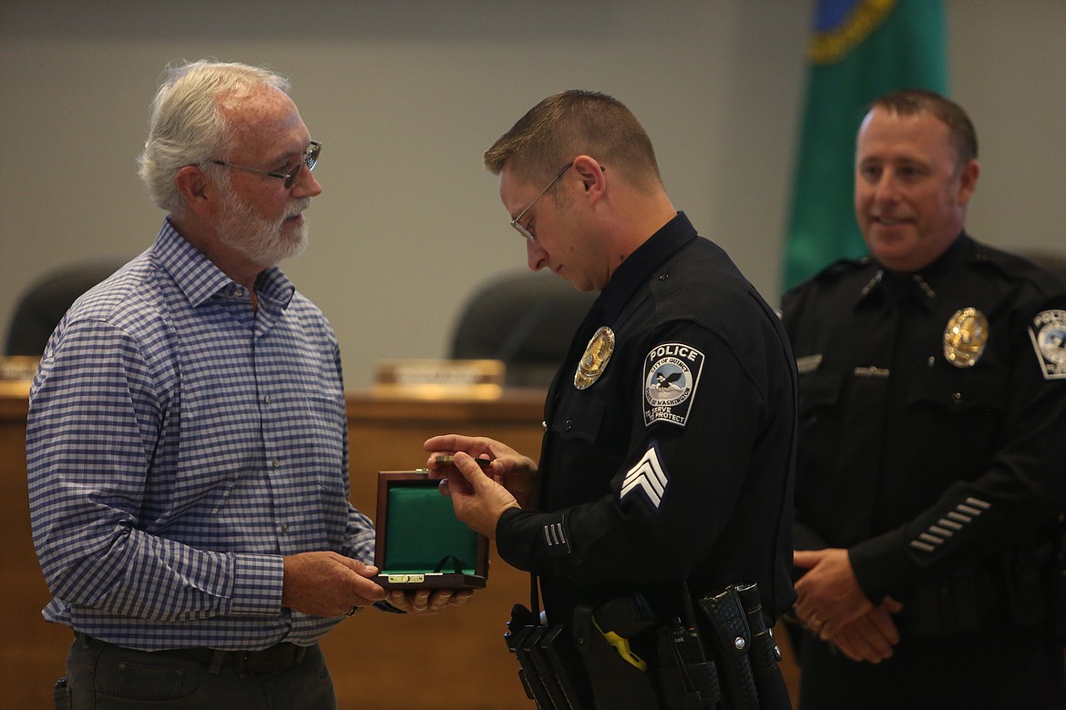 Quincy Police Department Sgt. Stephen Harder, center, inspects his newly-received Carnegie Hero Fund Medal after receiving the medal from U.S. Congressman Dan Newhouse, left.