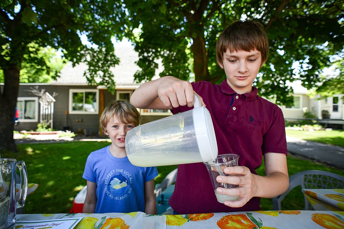 Maeson Linder, right, and Brennan Joy pour a cup of lemonade at their Hyper Lemonade stand along Sixth Avenue West as part of the Lemonade Day program on Saturday, June 22. (Casey Kreider/Daily Inter Lake)