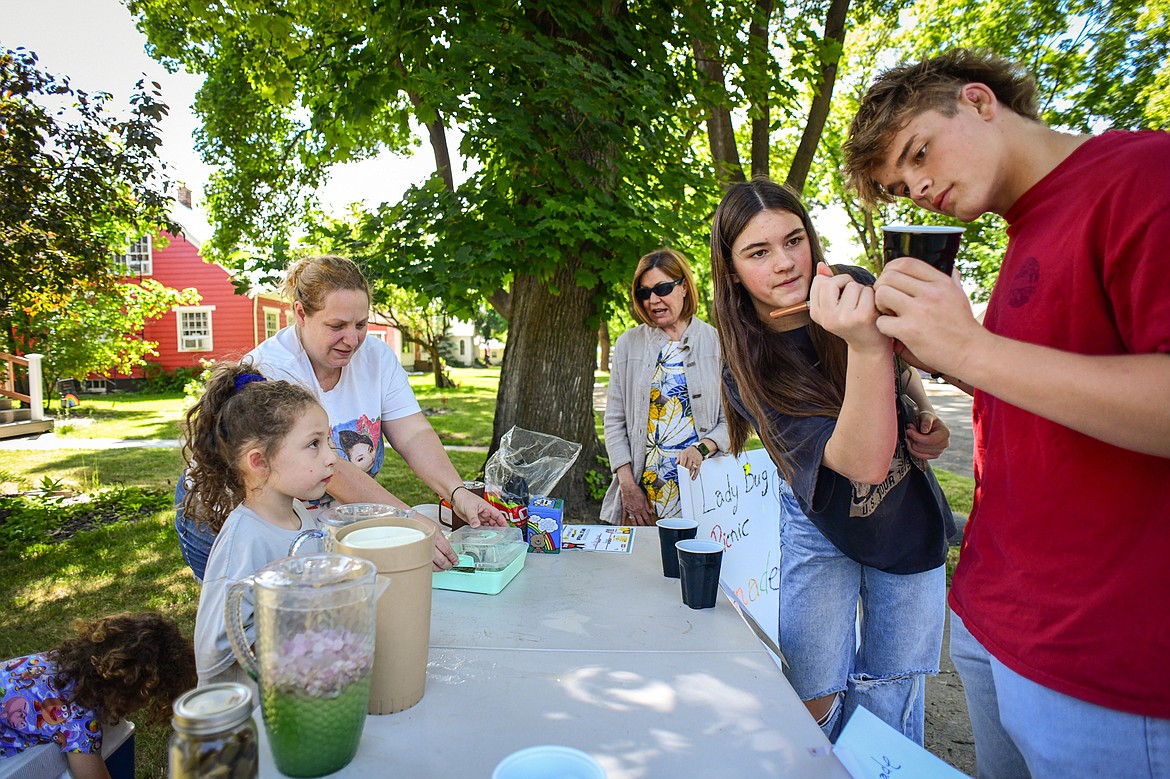 From left, Reagan Matheros, her mother Kendra Mathison and grandmother Karen Mathison serve lemonade to a couple customers at the Lady Bug Picnic stand as part of the Lemonade Day program on Saturday, June 22. (Casey Kreider/Daily Inter Lake)