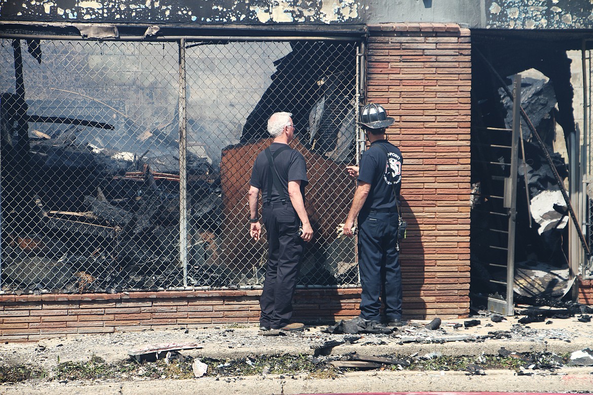 Army Surplus owner Cornel Rasor, left, is escorted to the front of what remains of his business by a Sandpoint firefighter Friday after the the building was destroyed in a July 4 fire.