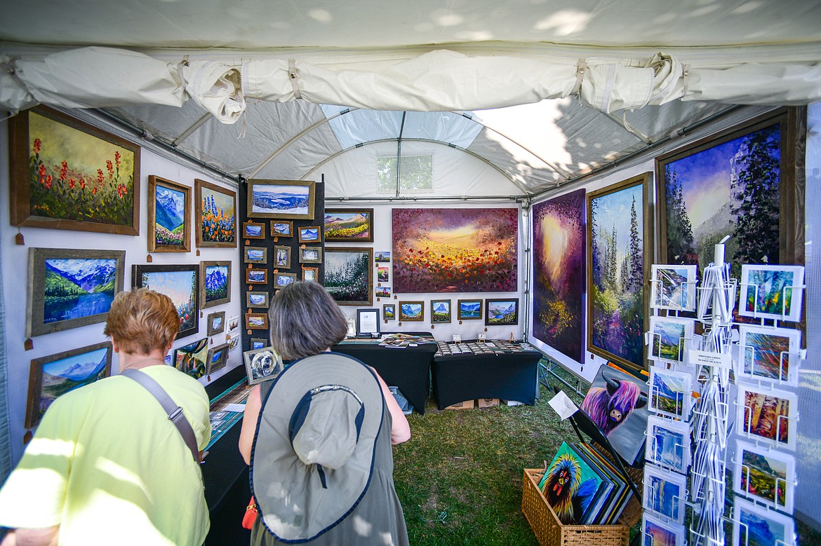 Two visitors look over the artwork at Kila resident Raette Meredith's Art by Raette stand at the Hockaday Museum's Arts in the Park at Depot Park in Kalispell on Friday, July 12. The event features over 80 art and craft booths, food trucks, a wine and beer garden, over 40 musical performers and community partner booths with free activities Friday, Saturday and Sunday July 12-14. (Casey Kreider/Daily Inter Lake)