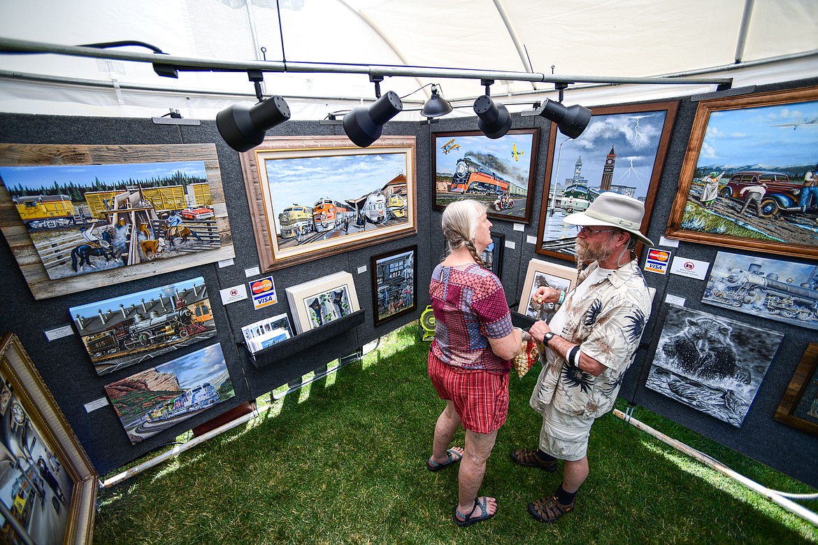 Sarah Burdick and Alan Roy look over the work of Shayne Stoakes in the Shayne's Fine Art & Custom Printing stand at the Hockaday Museum's Arts in the Park at Depot Park in Kalispell on Friday, July 12. The event features over 80 art and craft booths, food trucks, a wine and beer garden, over 40 musical performers and community partner booths with free activities Friday, Saturday and Sunday July 12-14. (Casey Kreider/Daily Inter Lake)