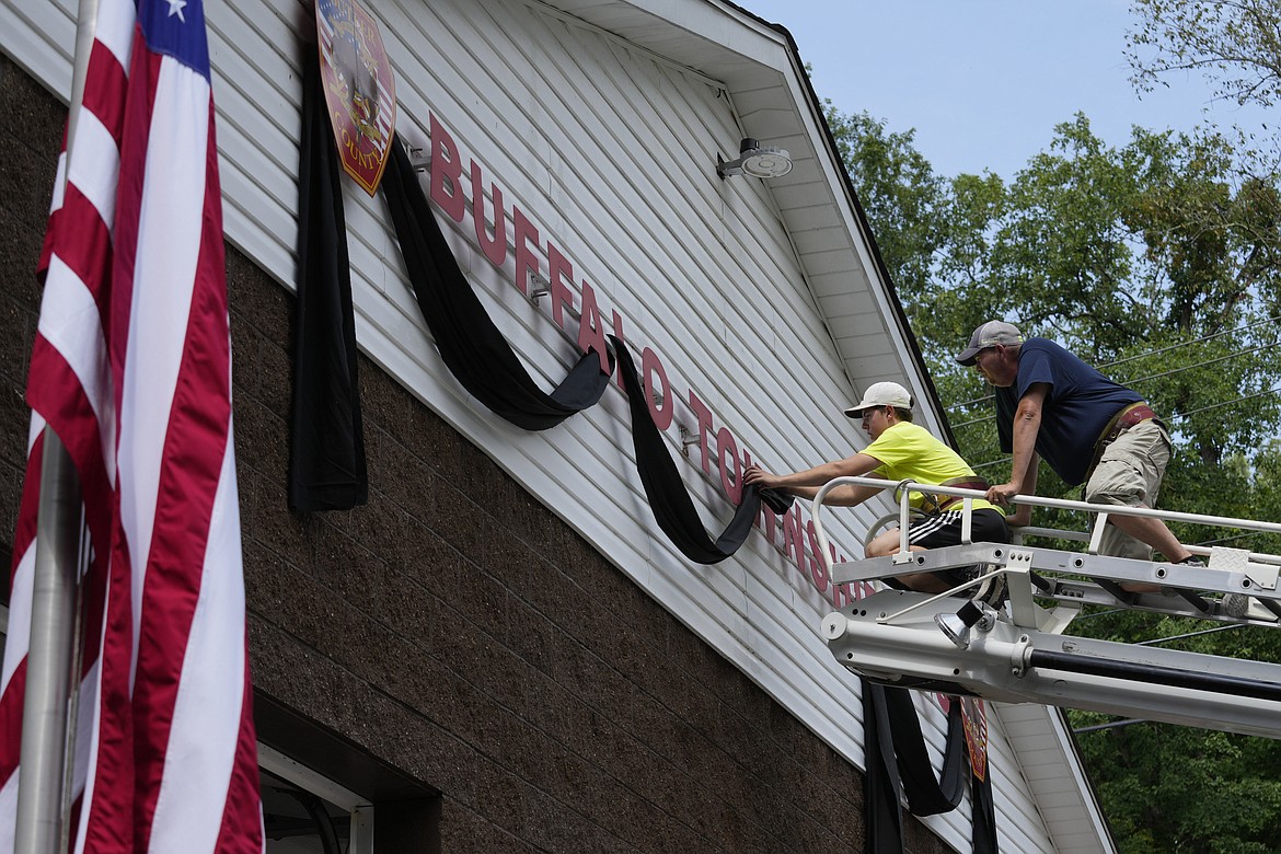 Logan Check, left, junior firefighter, and Randy Reamer, president and rescue captain at the Buffalo Township Fire Company 27, hang bunting on the fire station in memory of fellow firefighter Corey Comperatore, in Buffalo Township, Pa., Sunday, July 14, 2024. Comperatore was killed during a shooting at a campaign rally for Republican presidential candidate former President Donald Trump in Butler, Pa., on Saturday. The flag at the station house flies at half staff at left. (AP Photo/Sue Ogrocki)