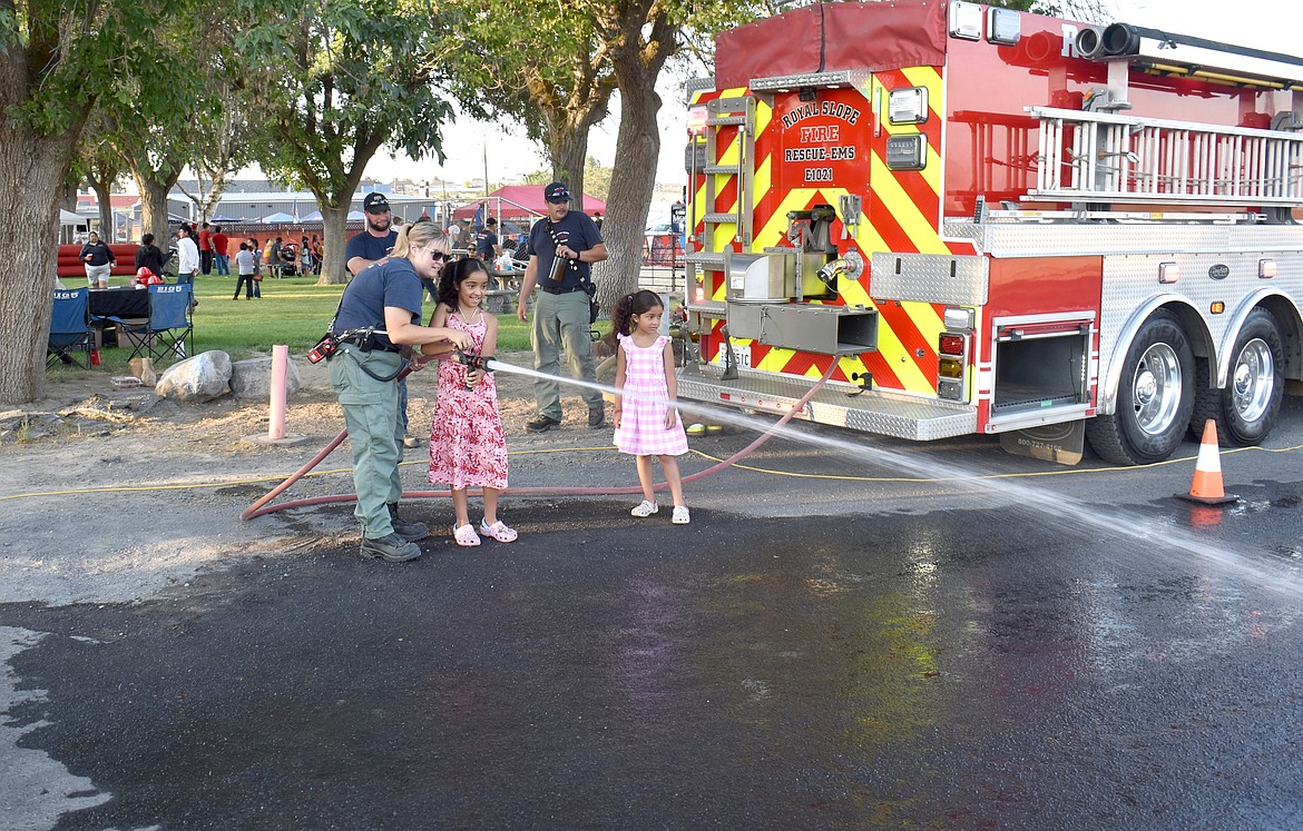 Enedina Torres, 10, of Royal City, uses a fire hose to knock over traffic cones with a little help from firefighter Samantha Sandstrom. Enedina’s little sister Evelia, 6, waits to try her hand next.