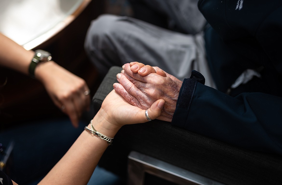 A veteran and caregiver hold hands during their visit to Normandy in June.