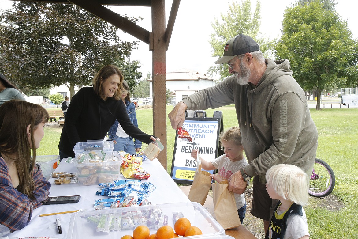 Ross Vincent of Athol reads a snack label as Bestowing the Basics volunteer Jennifer Lincoln offers him and his grandchildren Charlotte, 4, and Luke, 2, sandwiches and other goodies Tuesday in Athol City Park.